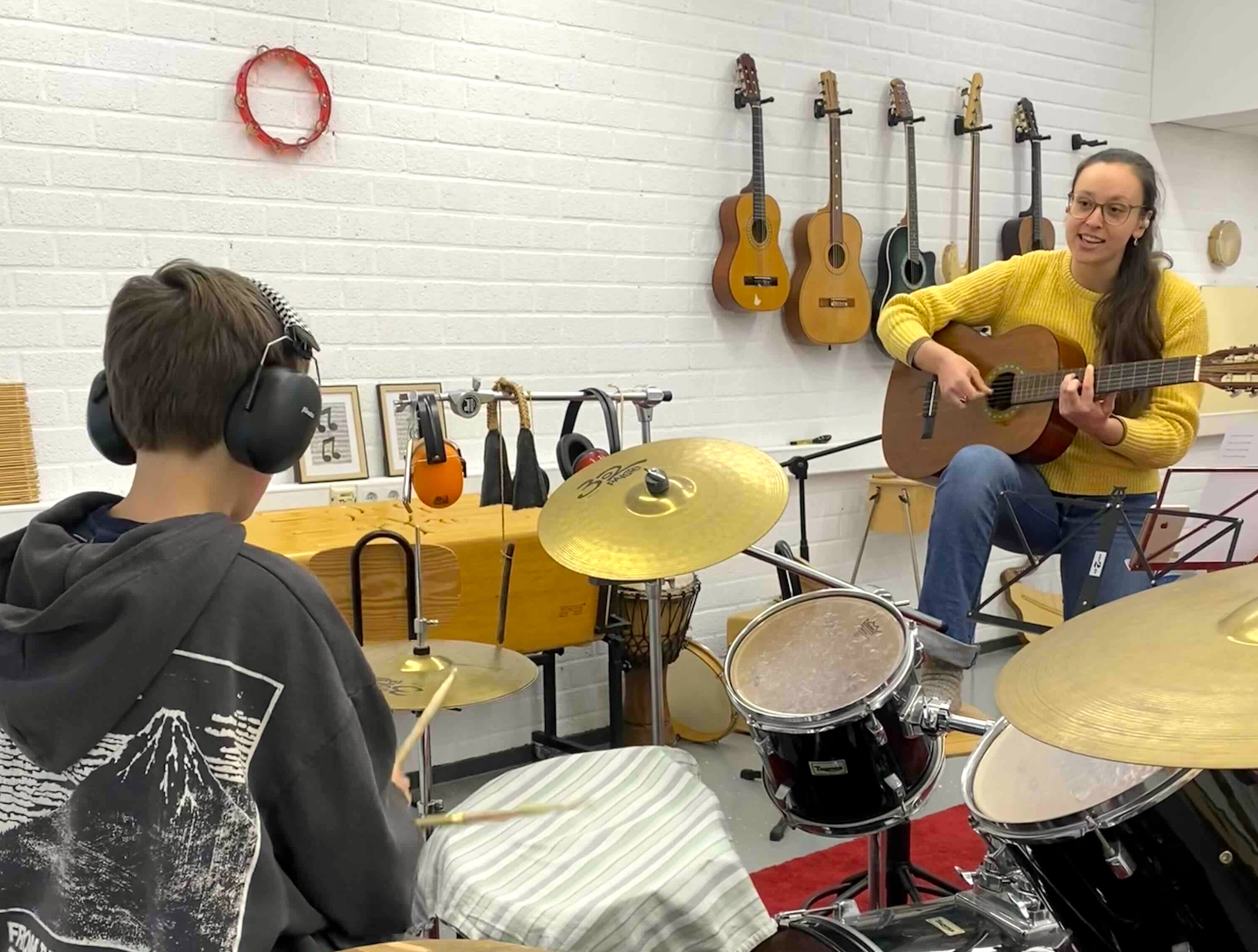 Foto van docent en leerling die gitaar en drum spelen