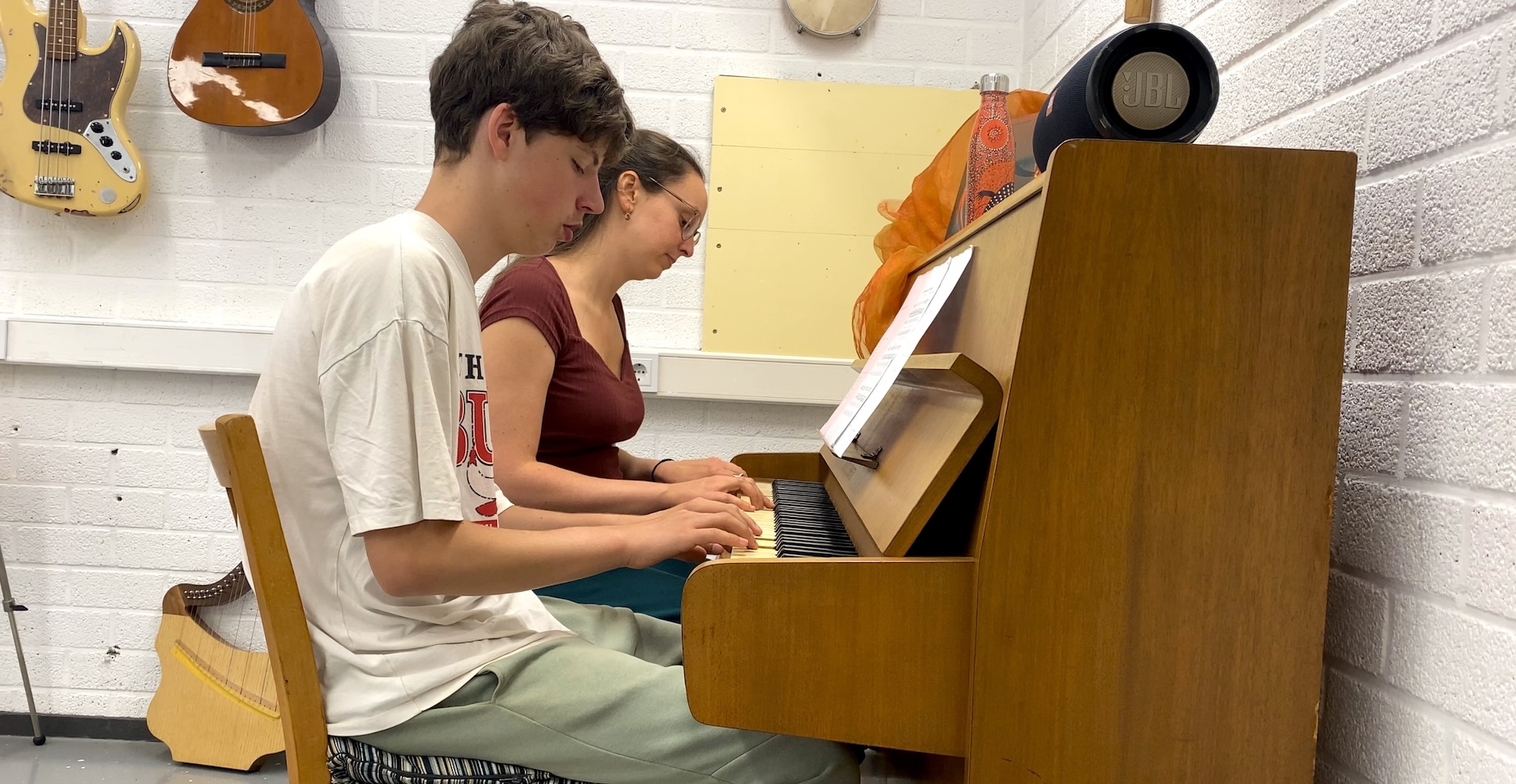 Foto van docent en leerling die piano spelen