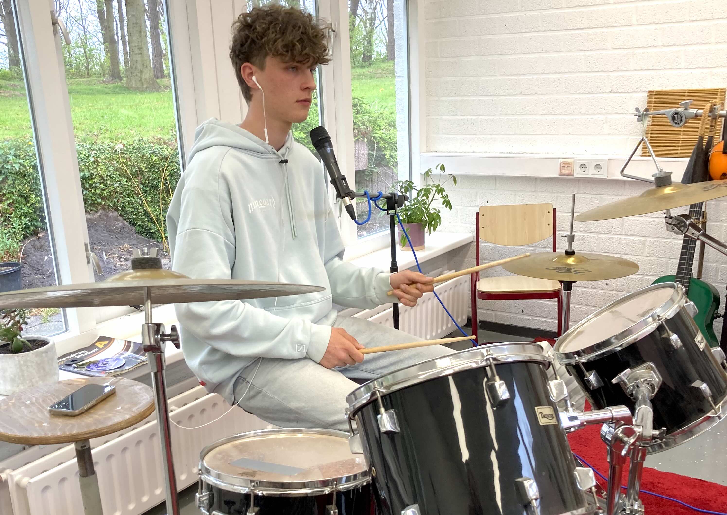 Foto van een leerling die zingt en drumt tegelijk