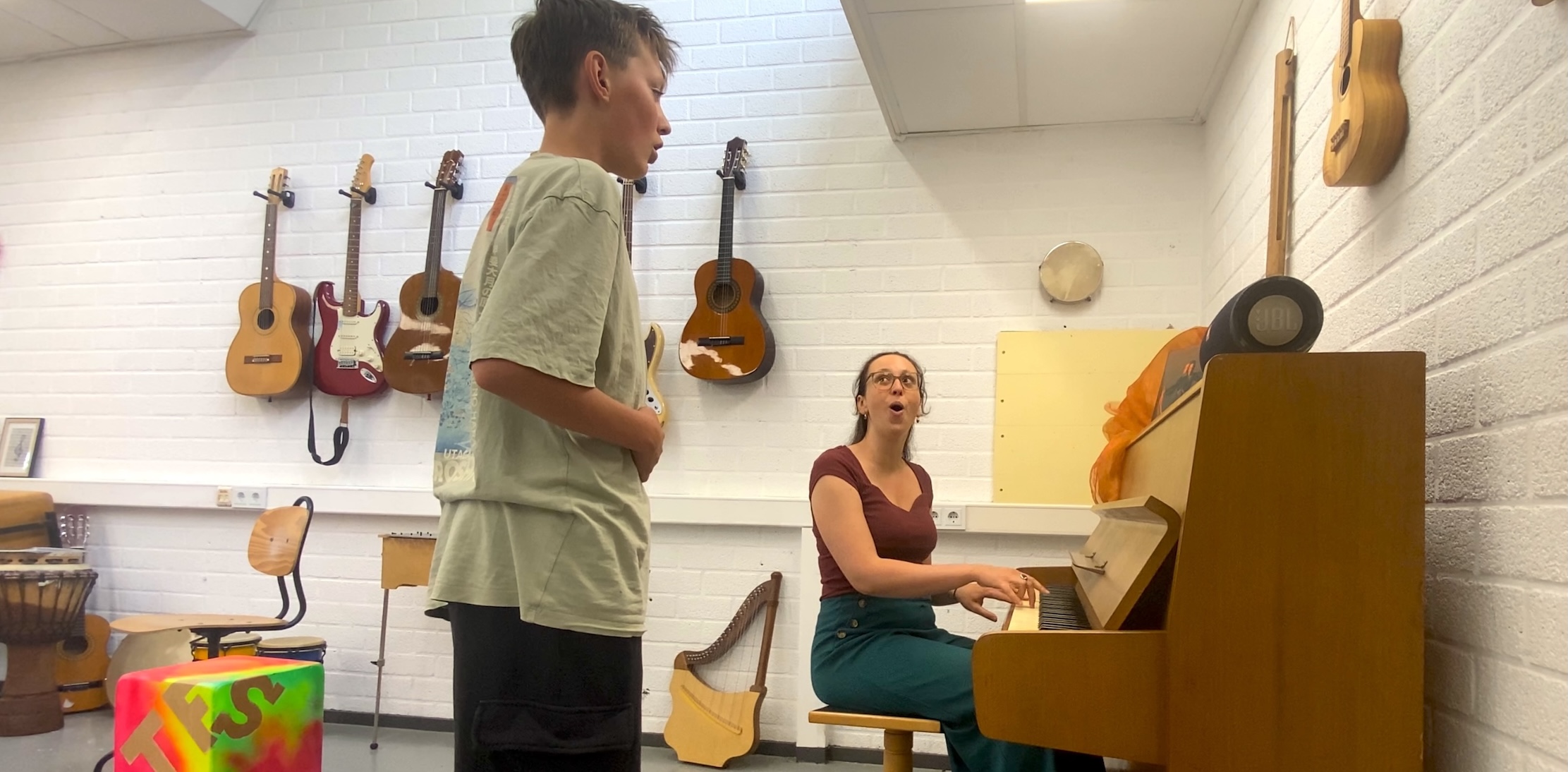 Foto van docent en leerling die zingen bij de piano